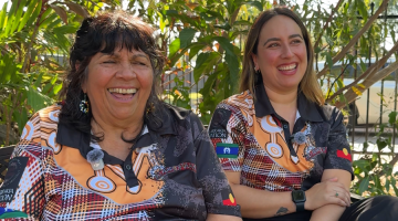 Two women sitting outside on a bench, smiling towards the camera.