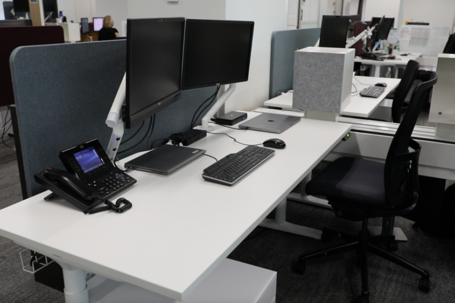 A work station with a desk, chair, computer screens, keyboard and telephone.